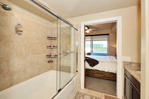 Full bath with vanity, combined bath / shower with glass door, ensuite bath, light tile patterned floors, and a ceiling fan