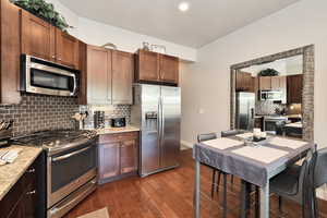 Kitchen featuring appliances with stainless steel finishes, light stone counters, tasteful backsplash, and dark wood finished floors