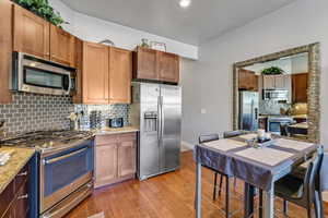 Kitchen featuring stainless steel appliances, backsplash, brown cabinets, and light wood-type flooring
