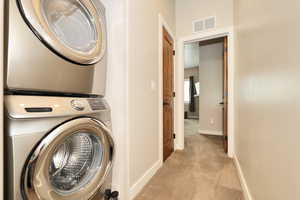 Washroom featuring light colored carpet and stacked washer / drying machine