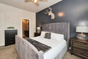 Bedroom with light carpet, ensuite bathroom, and ceiling fan