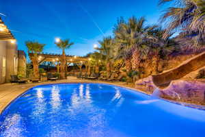 Pool at dusk featuring an outdoor pool, a water slide, a patio, and a pergola
