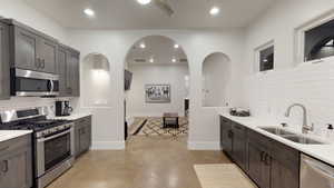 Kitchen with decorative backsplash, stainless steel appliances, arched walkways, light stone counters, and recessed lighting