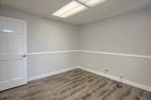 Empty room with a drop ceiling, wood finished floors, and a wainscoted wall