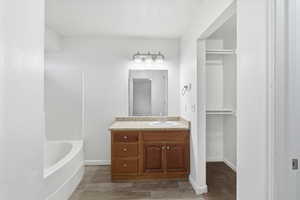 Full bath featuring vanity, a spacious closet,  shower combination, and dark wood-type flooring