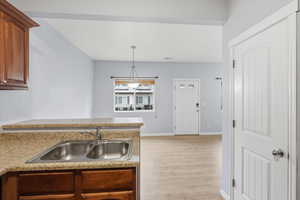 Kitchen with a peninsula, light countertops, pendant lighting, light wood finished floors, and brown cabinetry
