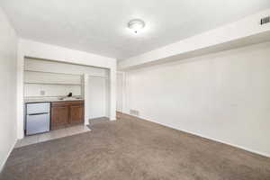 Bar area featuring light countertops, stainless steel refrigerator, light colored carpet, and brown cabinetry