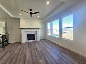 Unfurnished living room with a raised ceiling, dark wood finished floors, ceiling fan, recessed lighting, and a fireplace