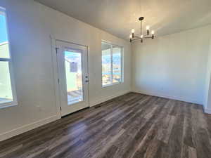 Unfurnished dining area featuring dark wood-style flooring, a textured ceiling, and a chandelier