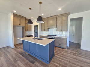 Kitchen featuring decorative light fixtures, an island with sink, recessed lighting, backsplash, and gas range
