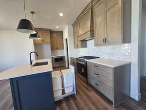 Kitchen with stainless steel appliances, hanging light fixtures, dark wood-style floors, an island with sink, and custom exhaust hood