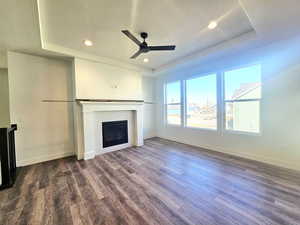 Unfurnished living room with a tray ceiling, a tile fireplace, dark wood-style floors, a textured ceiling, and a ceiling fan