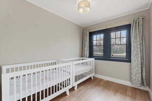 Bedroom with light wood finished floors, crown molding, and a nursery area