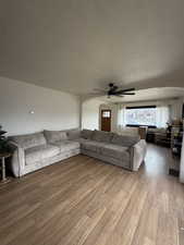 Living room with arched walkways, a textured ceiling, wood finished floors, and ceiling fan