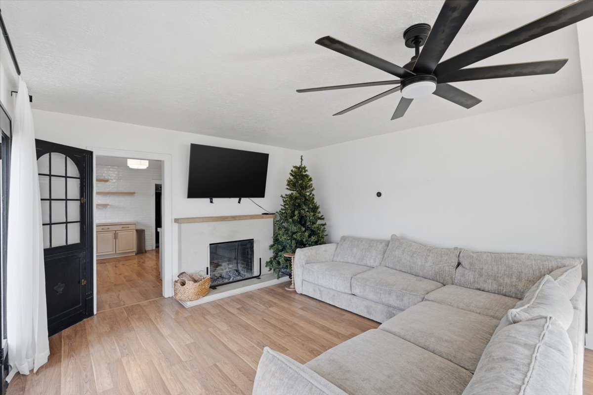Living area with light wood-type flooring, a glass covered fireplace, and ceiling fan