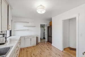Kitchen with open shelves, light wood-style flooring, freestanding refrigerator, backsplash, and white cabinetry