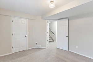 Finished basement with light colored carpet and stairs