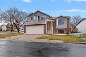 Tri-level home featuring brick, siding, driveway, a garage, a front lawn, and roof with shingles