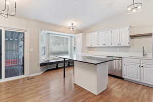 Kitchen featuring white cabinets, lofted ceiling, dishwasher, large island, a chandelier, and light wood-type flooring