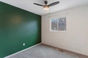 Carpeted spare room featuring ceiling fan and baseboards