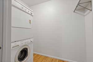 Washroom with stacked washer / dryer and light wood-type flooring