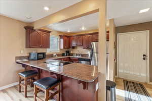 Kitchen featuring a kitchen bar, a peninsula, black appliances, and dark stone countertops