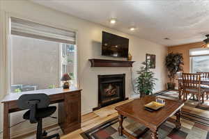 Living room with a fireplace with raised hearth, healthy amount of natural light, a ceiling fan, a desk, and a textured ceiling