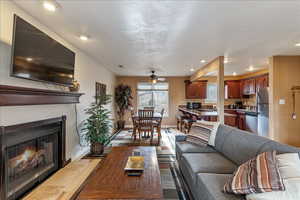 Living room with a warm lit fireplace, recessed lighting, a ceiling fan, a textured ceiling, and light wood finished floors