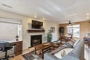 Living area featuring a fireplace, light wood finished floors, a textured ceiling, a ceiling fan, and recessed lighting