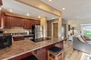 Kitchen with a breakfast bar, light stone counters, a peninsula, appliances with stainless steel finishes, and light wood-style floors