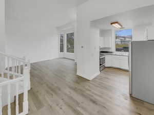 Kitchen with stainless steel appliances, white cabinets, light wood finished floors, light countertops, and open floor plan