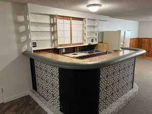 Kitchen with wood walls, a wainscoted wall, a textured ceiling, white fridge with ice dispenser, and dark wood finished floors