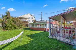 View of green lawn featuring a wooden deck and a sunroom