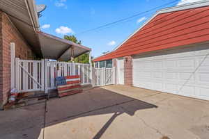 View of side of home with a patio area, a gate, brick siding, and a garage