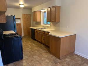 Kitchen featuring black appliances, light countertops, stone finish floors, and brown cabinetry