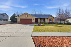 Ranch-style home with driveway, stucco siding, brick siding, covered porch, and a garage