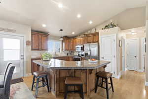Kitchen featuring a breakfast bar, appliances with stainless steel finishes, vaulted ceiling, brown cabinets, and pendant lighting