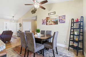 Dining space with wood finished floors, ceiling fan, and high vaulted ceiling