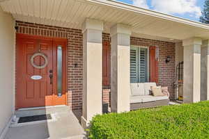 View of exterior entry featuring covered porch and brick siding