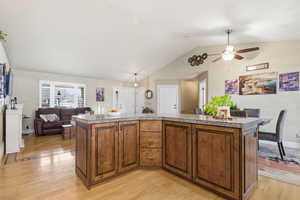 Kitchen with tile countertops, brown cabinets, vaulted ceiling, open floor plan, and a center island