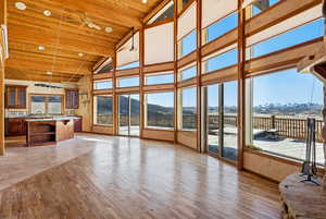 Unfurnished living room with high vaulted ceiling, light wood-type flooring, a mountain view, a wooden ceiling with exposed beams, and a ceiling fan