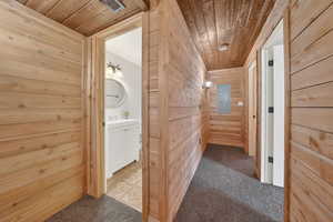 Corridor with wood walls, carpet flooring, wood ceiling, and electric panel