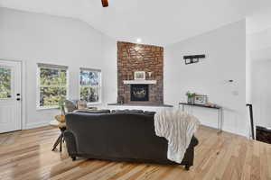 Living area featuring a stone fireplace, light wood-style floors, ceiling fan, and high vaulted ceiling