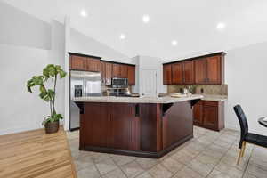 Kitchen with a kitchen bar, stainless steel appliances, lofted ceiling, decorative backsplash, and light granite countertops