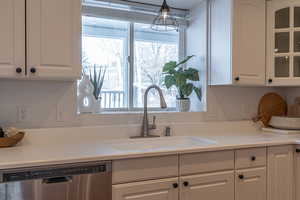 Kitchen with white cabinetry, dishwasher, light countertops, and glass insert cabinets