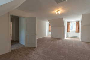 Bonus room with a textured ceiling, light colored carpet, and baseboard heating