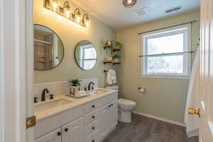 Full bath with double vanity, dark wood-style floors, healthy amount of natural light, a textured ceiling, and a shower with shower curtain