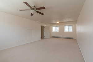 Empty room featuring light colored carpet, a baseboard radiator, a textured ceiling, and a ceiling fan