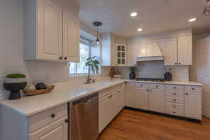 Kitchen featuring appliances with stainless steel finishes, a textured ceiling, light countertops, custom exhaust hood, and dark wood finished floors