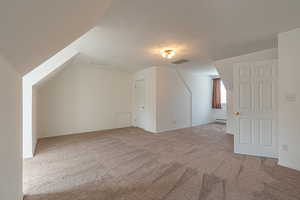Additional living space with light carpet, a textured ceiling, and a baseboard heating unit